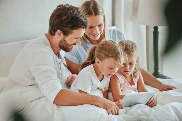 Happy, family and tablet for entertainment on the bed watching shows together while relaxing at home. Mother, father and children relax with smile for online streaming on touchscreen in the bedroom.