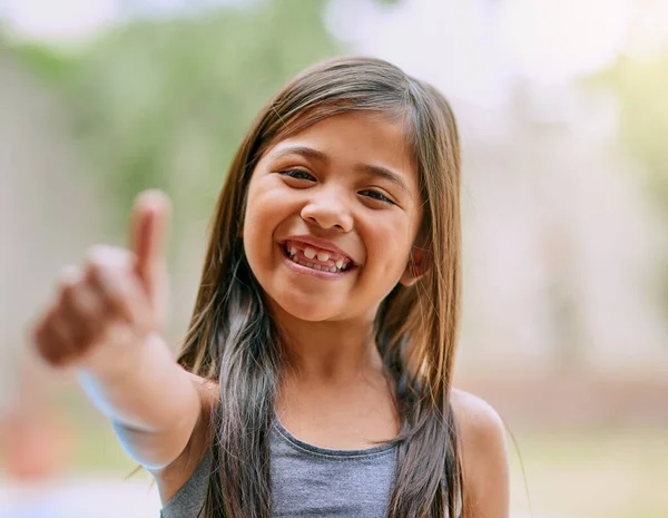 Childhood should be filled with big smiles and happy days. Portrait of a little girl showing thumbs up outside