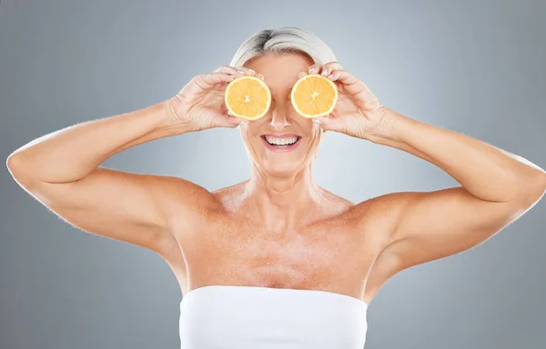 Beauty, skincare and orange with a model mature woman in studio on a gray background for health or wellness. Food, fruit and natural with an elderly female posing to promote nutrition or luxury.