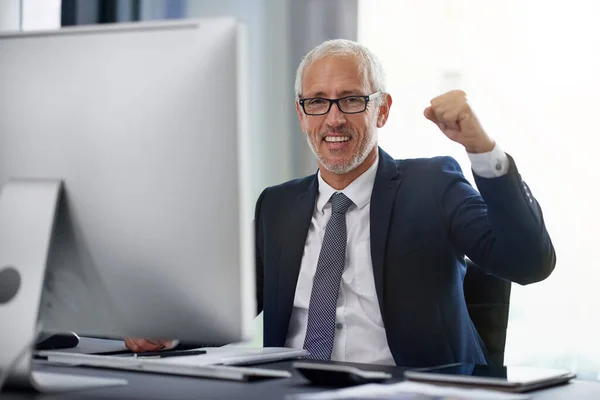 Another day, another win. Portrait of a smiling mature businessman doing a fist pump while sitting at his desk in an office