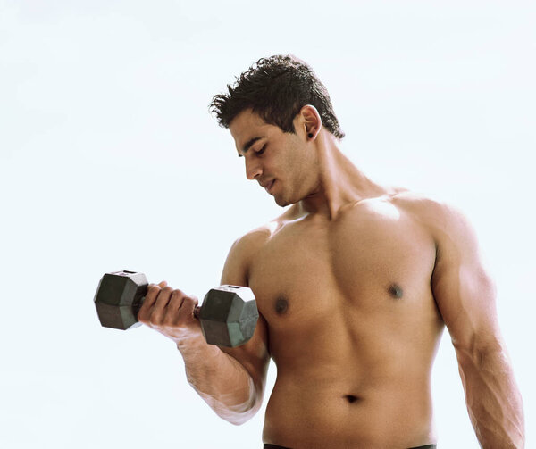 Go heavy or go home. a shirtless young man working out with dumbbells outside