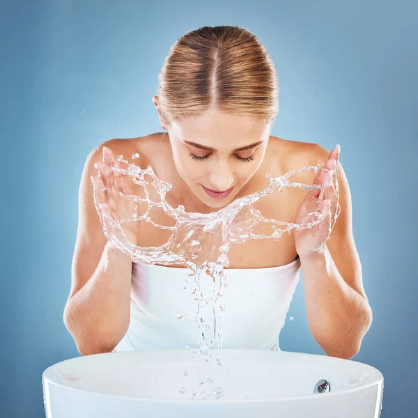 Woman, water or washing face in grooming skincare on blue background studio from sink or basin. Beauty model, wet and facial cleaning with water splash for hygiene maintenance, healthcare or wellness.