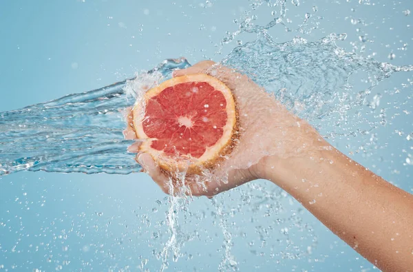 Fruit, water and hand splash for beauty, care and healthy skincare and bodycare on a blue studio background. Grapefruit, hands and hygiene with vitamin c for organic and natural body skin cleansing.
