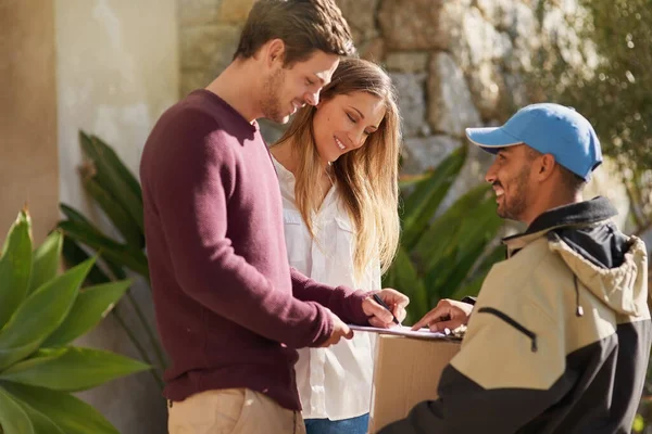 I just need your name right here. a courier delivering a package to a smiling young couple at home