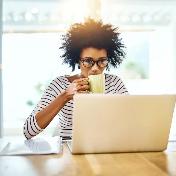 stock image Time to get started. a focused young woman working on a laptop and drinking coffee at home