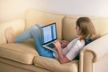 Makaleyi son bir kez daha okuyacağım. Genç bir kadın evdeki kanepede otururken bilgisayarını kullanıyor.