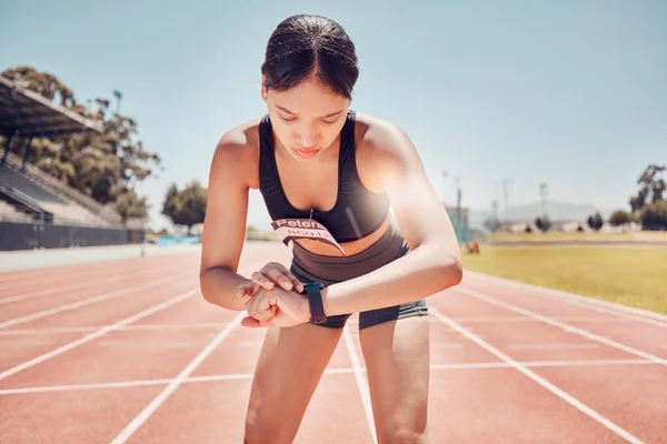 Smartwatch, sports and woman check time, workout goal or progress during training, running or exercise at stadium in summer. Runner, athlete or fitness girl with smart watch or workout technology app.