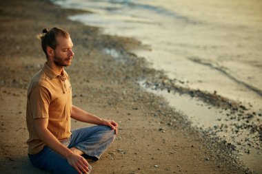 Ruhunu dinle, neye ihtiyacı olduğunu biliyor. Sahilde yoga yaparken lotus pozisyonunda oturan bir adam.