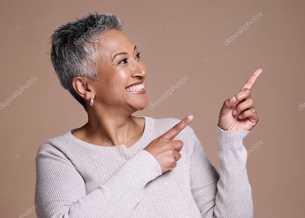 Mature woman pointing to space on studio background for marketing, advertising or presentation of ideas, choice and review. Happy lady showing brown mockup, offer and branding of commercial promotion.