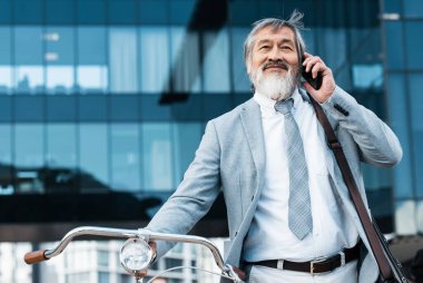 Bisiklet, telefon ve Asyalı işadamı telefonda konuşuyor, konuşuyor ve dinliyor. Seyahat, çevre dostu ulaşım ve düşük karbon ayak izi için akıllı telefonu ve bisikleti olan olgun Asyalı adam..