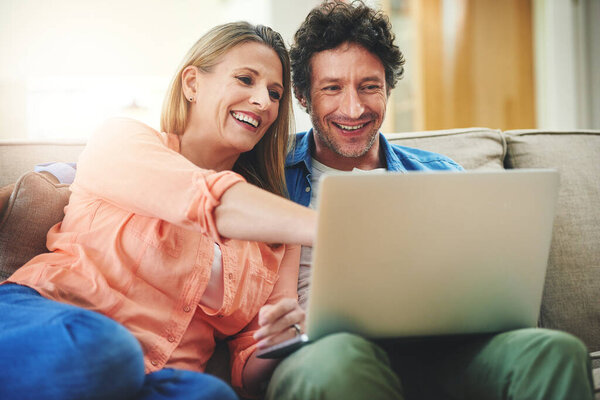 Lets watch this movie. a happy mature couple using a laptop together on the sofa at home
