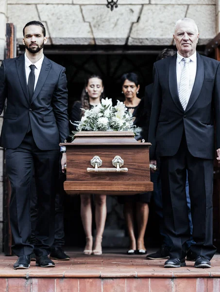 stock image Funeral, church and people with a coffin, family and mourning in emotional distress. Church service, casket and burial with sad men and women carrying dead person together out of a chapel door.