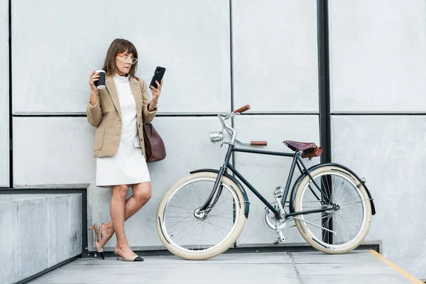 Business woman, phone and coffee with bicycle for eco friendly transport for travel on city break while online with 5g network. Entrepreneur on break using mobile app for communication and networking.