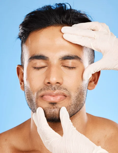 Plastic surgery, man and cosmetics for face, skincare or natural beauty against blue studio background. Young male, white gloves or organic facial for smooth, glow skin and hydration for rejuvenation.