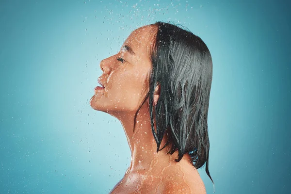 Woman, hygiene and wet shower for relax, beauty or fresh clean with water drops against a blue studio background. Relaxed female enjoying a hygienic wash and liquid sensation in cleanliness on mockup.