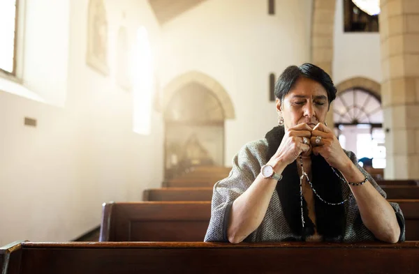 Pray, church and senior woman praying with a rosary in a calm, zen chapel alone, holy and spiritual. Prayer, worship and mexican lady connect with God, Jesus and christian religion in Mexico.