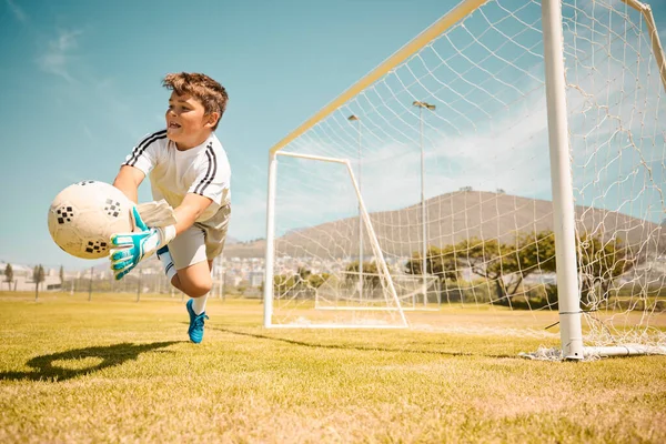 Football, boy goalkeeper and jump, saving ball from goals at outdoor sports field. Soccer, kid and competition game with fitness, goal keeper and soccer ball on grass, success and action to save goal.