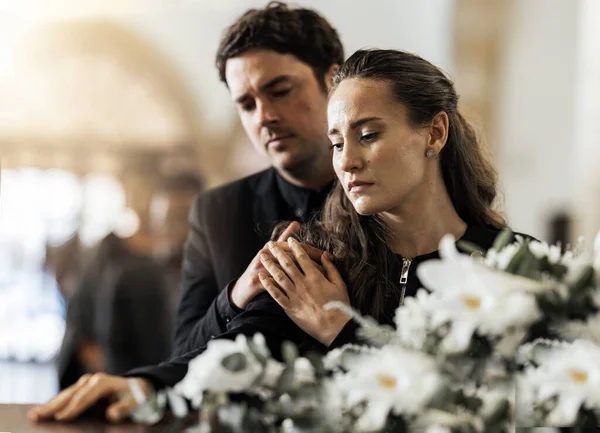 Sad, funeral and flowers with couple and coffin in church for death, respect and mourning. Grief, goodbye and empathy with man and woman loss at casket with depression, remember and farewell memorial.