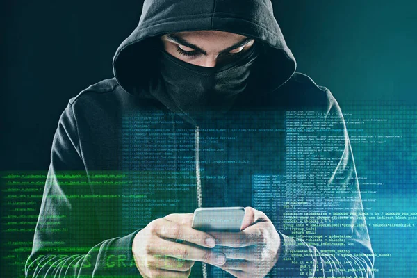 This hacker moves with the times. a computer hacker using a smartphone while standing against a dark background