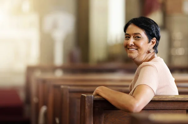Senior woman, christian and happy in church, spiritual and religion after service, smile and lifestyle. Elderly female smile, portrait and empowerment while sitting in wood bench in catholic chapel.