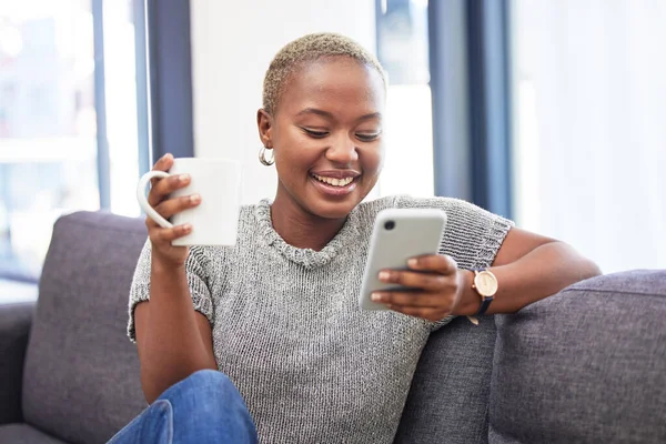 打电话 在沙发上休息 喝咖啡 早上例行滚动社交媒体 快乐的非洲女孩 在智能手机上流连忘返 在客厅喝茶的沙发上阅读数字5G通讯 — 图库照片