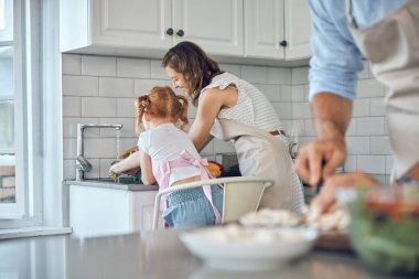 Anne ve kızıyla birlikte mutfakta sebze yıkamak, yemek yapmak ve malzemeleri birlikte temizlemek. Aile, yardım ve sağlık. Yemekten önce lavabo lavabosuyla temizlik yapan bir kadın ve kız..