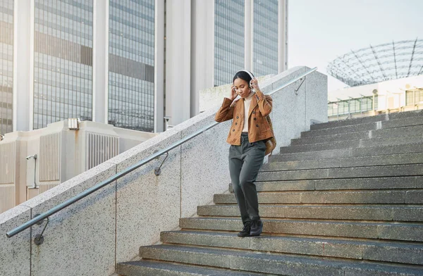 Music, stairs and city with a business black woman walking outdoor while using headphones for streaming audio. Steps, commute and listening with a female employee streaming audio in an urban town.