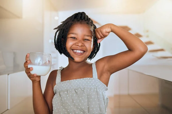 Milk, portrait and African girl with muscle from healthy drink for energy, growth and nutrition in the kitchen. Happy, smile and child flexing muscles from calcium in a glass and care for health.