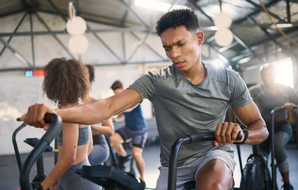 Gym, fitness and man on a spinning bike for exercise, health and cross training, power and motivation. energy, spinning bike and black man on air bike and sports center for wellness, workout and fit.