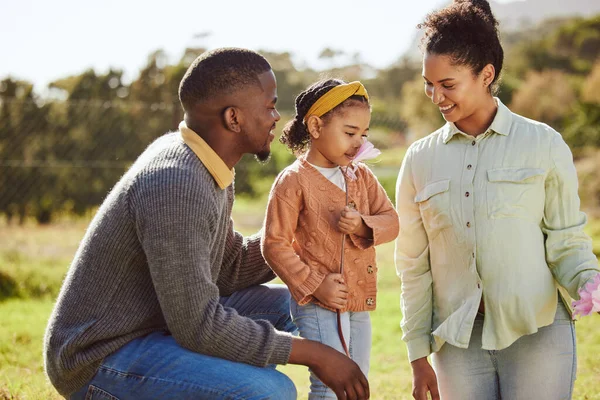 Happy family, nature and child smell flowers while relax in countryside Spring field with mother, father or parents. Love, freedom peace or harmony for black man, woman and kid girl with floral plant.