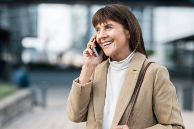 İletişim, telefon görüşmesi ve şehirdeki olgun bir kadının konuşması, internette konuşması. Teknoloji, bağlantı ve şehir merkezinde akıllı telefon kullanan, gülümseyen ve mutlu bir kadın..