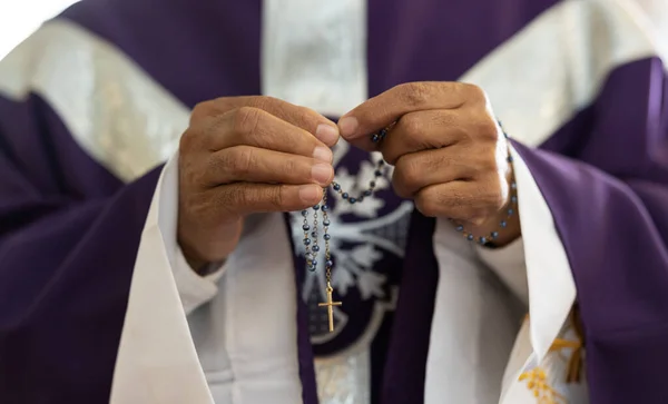 Priest, pastor and man hands with rosary with cross in church, prayer and catholic worship, praying or spiritual respect. Christian preacher, faith beads with crucifix and holy religion for God mercy.