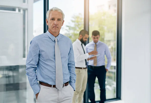 We share the same ambitious drive. Portrait of a mature businessman standing in an office with colleagues in the background