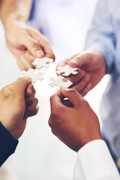 Putting the pieces together. Closeup shot of a group of unidentifiable businesspeople holding puzzle pieces together