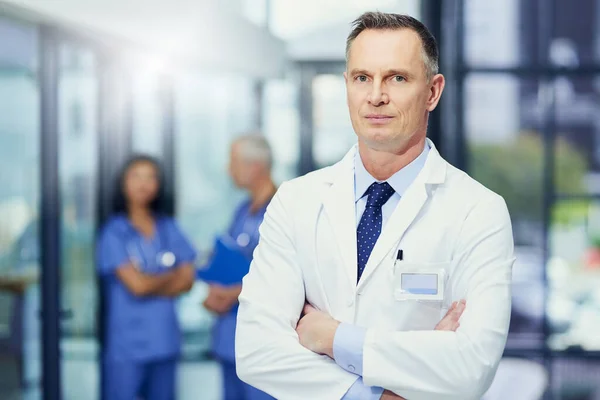 Focused on saving lives. Portrait of a mature male doctor standing in a hospital with colleagues in the background