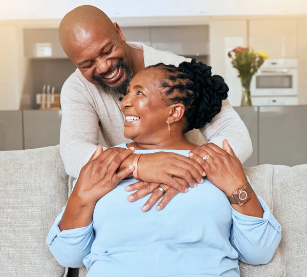 シニアブラックカップル 抱擁と笑顔でソファ 家庭での愛や幸福 リビングルームや一緒にリラックス 高齢者幸せなカップル アフリカ人とソファで抱擁 ラウンジケア ロマンスや結合 — ストック写真