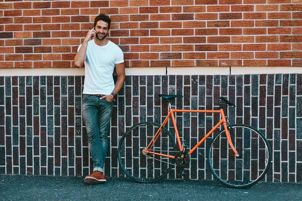 镇上最酷最有关系的人一个英俊的年轻人站在他的自行车旁边 在城里用电话 — 图库照片
