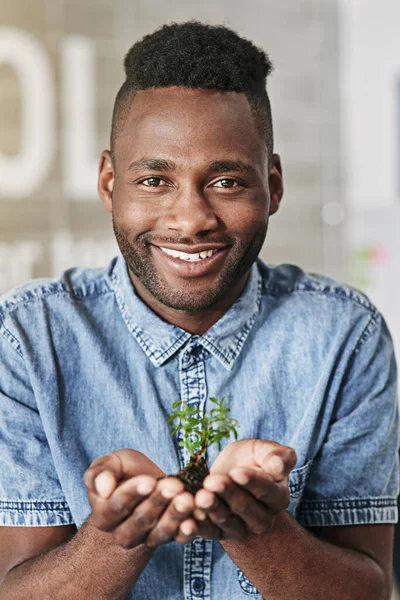 Growing my business. Watch this space. Portrait of a young man holding a plant growing out of soil in a modern office