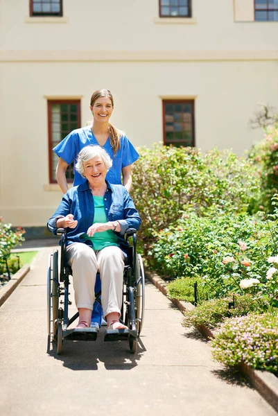 庭を通って彼女を押してください 老人ホームの庭の外の住人と看護師 — ストック写真