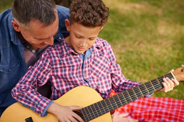 Strumming a tune with dad. a father teaching his son how to play guitar while sitting outside