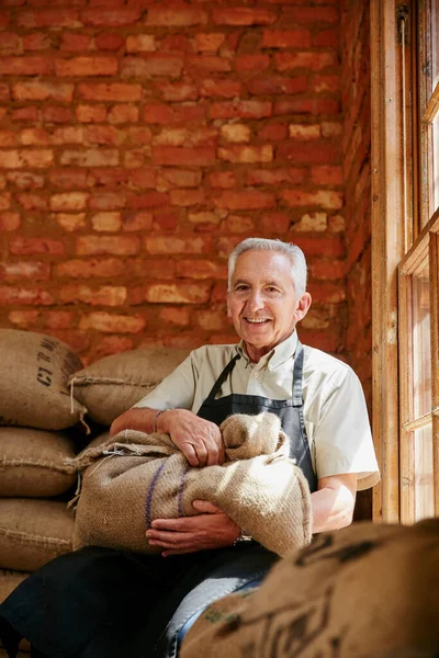These beans are ready for brewing. Cropped portrait of a senior man holding a sack of coffee beans while sitting in a roastery