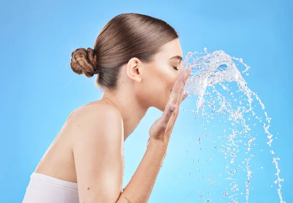 Skincare, water and woman cleaning face in studio on blue background for wellness, hygiene and facial cleanse. Beauty, hydration and girl washing skincare products, cosmetics and makeup with splash.