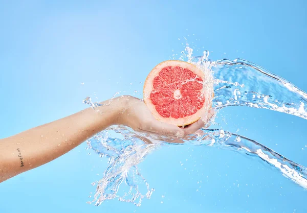 Hands, fruit and water splash for skincare wellness, cosmetics or nutrition against a blue studio background. Hand holding grapefruit for clean hygiene, hydration or vitamin C for body cleansing.