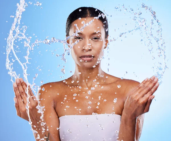 Portrait, water splash and skincare woman for beauty, moisture or self care by blue background. Black woman, skin model and cleaning face for health, dermatology or wellness with natural cosmetics.