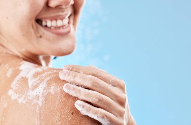 Sağlık, cilt bakımı ve sağIığı için vücudu hazırlayan bir kadının duşu, sabunu ve gülüşü mavi bir model stüdyo arka planına karşı. Su, temizlik ve omzu köpüklü bir modelin eli ve mekanı taklit eder..