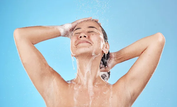 Beauty, hair and woman in shower happy on blue background, haircare and hygiene routine in the morning. Model in water with shampoo foam, cleaning hair with running water for clean fresh lifestyle