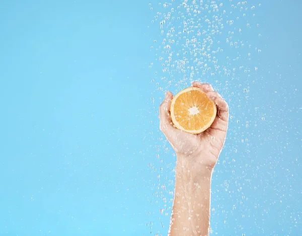 Hand, orange and water with natural skincare for health, wellness and organic fruit on a blue studio background. Beauty, fresh and food for juicy vitamin c skin care treatment for dermatology.