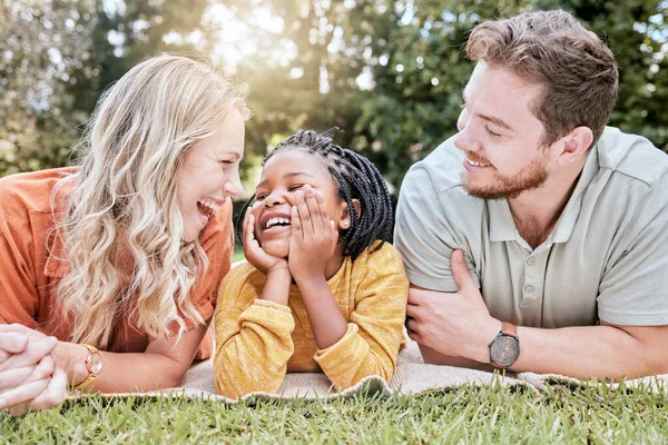 Family, adoption and picnic on blanket in park with mother, father and black girl in nature, relax and happy. Diversity, kid and parents relaxing on grass in the yard, enjoy summer with love or smile.