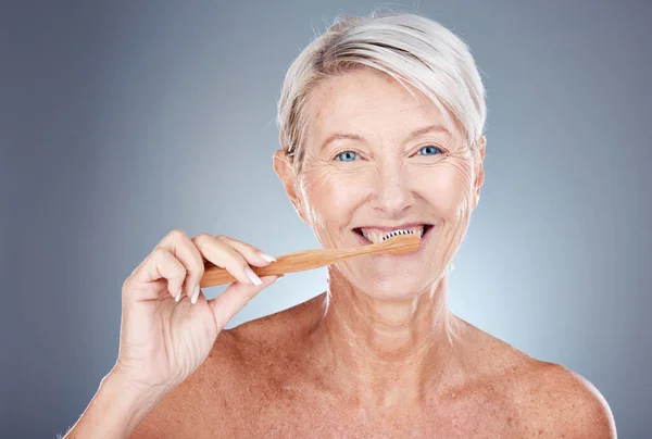 Mature woman, toothbrush and portrait for health, wellness and oral care on a grey studio background. Brushing teeth, clean and senior female cleaning her mouth for oral care or dental hygiene.