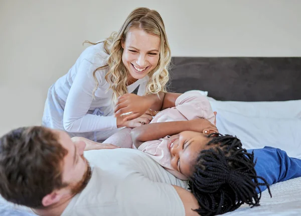 Foster parents tickle adoption kid in bedroom, family home and house for fun, bonding and quality time with love, care and happiness together. Happy black kid relax with mom, dad and diversity people.